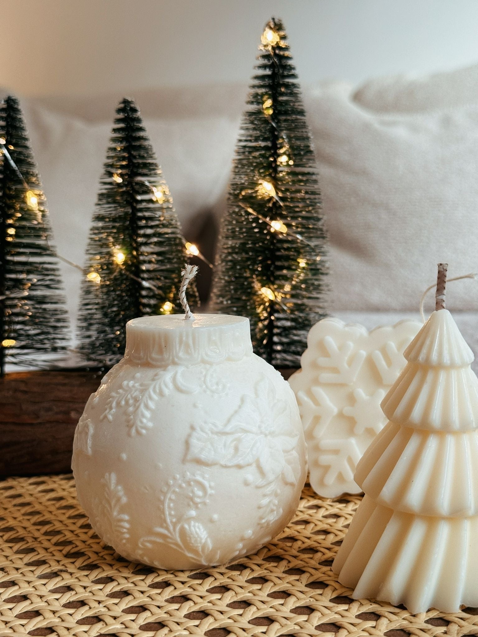 Decorative candles shaped like Christmas trees and ornaments on a textured surface with a snowy background.