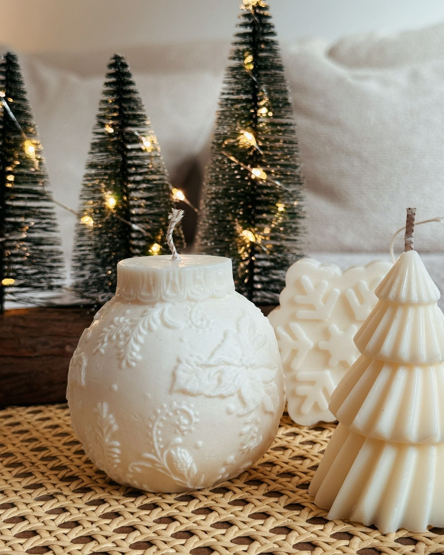 Decorative candles shaped like Christmas trees and ornaments on a textured surface with a snowy background.