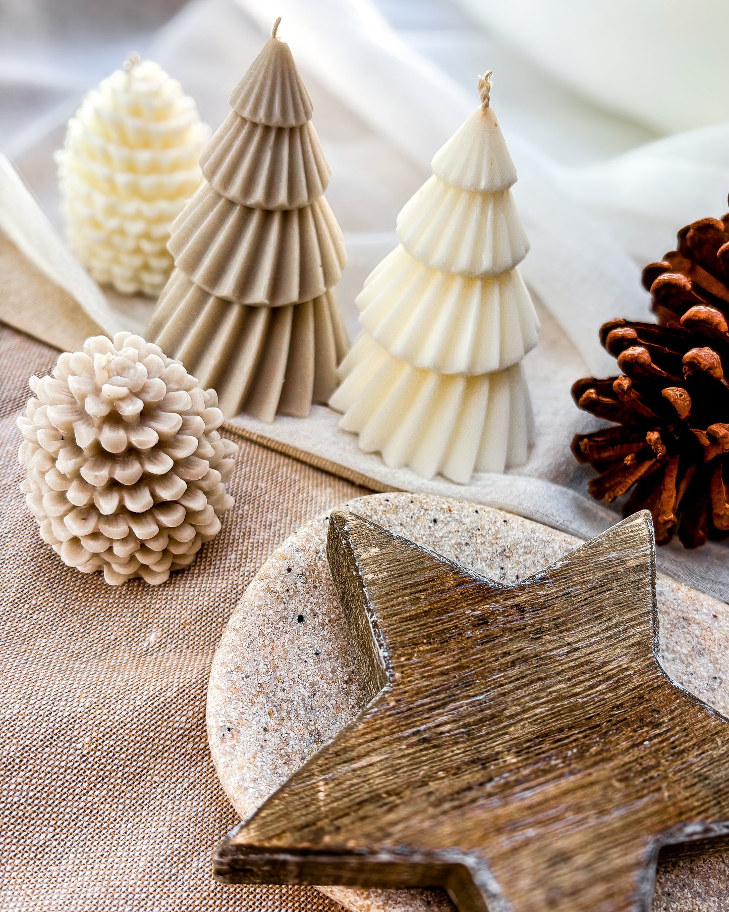 Wooden star, tree-shaped candles, and pinecones on a textured surface