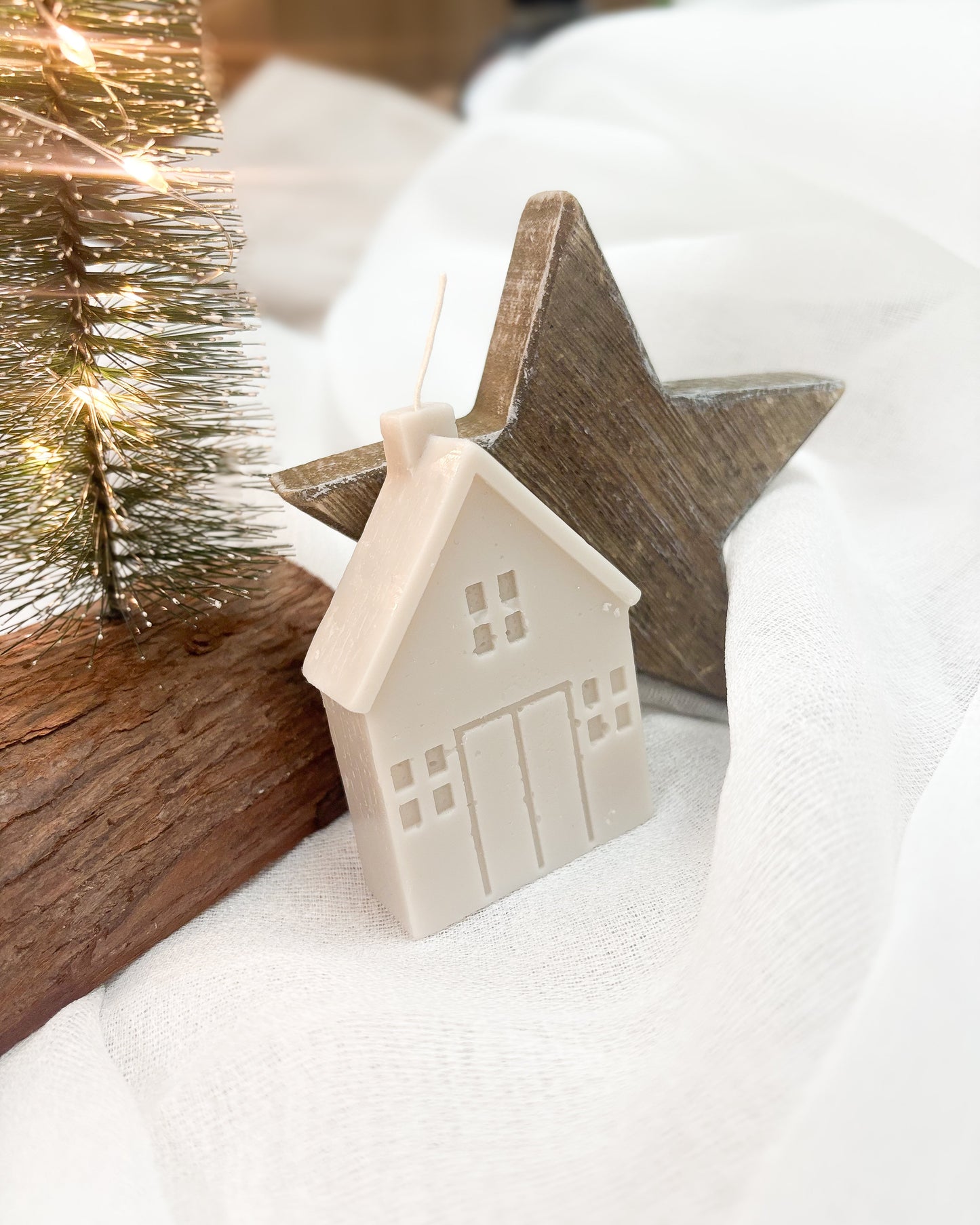 Small house ornament and wooden star on a white surface with blurred festive background