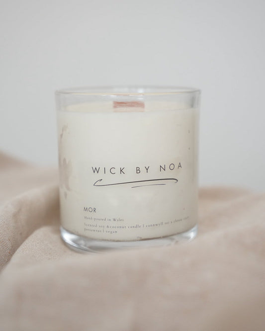 Candle in a glass jar with 'Wick by Noa' label on a soft fabric background