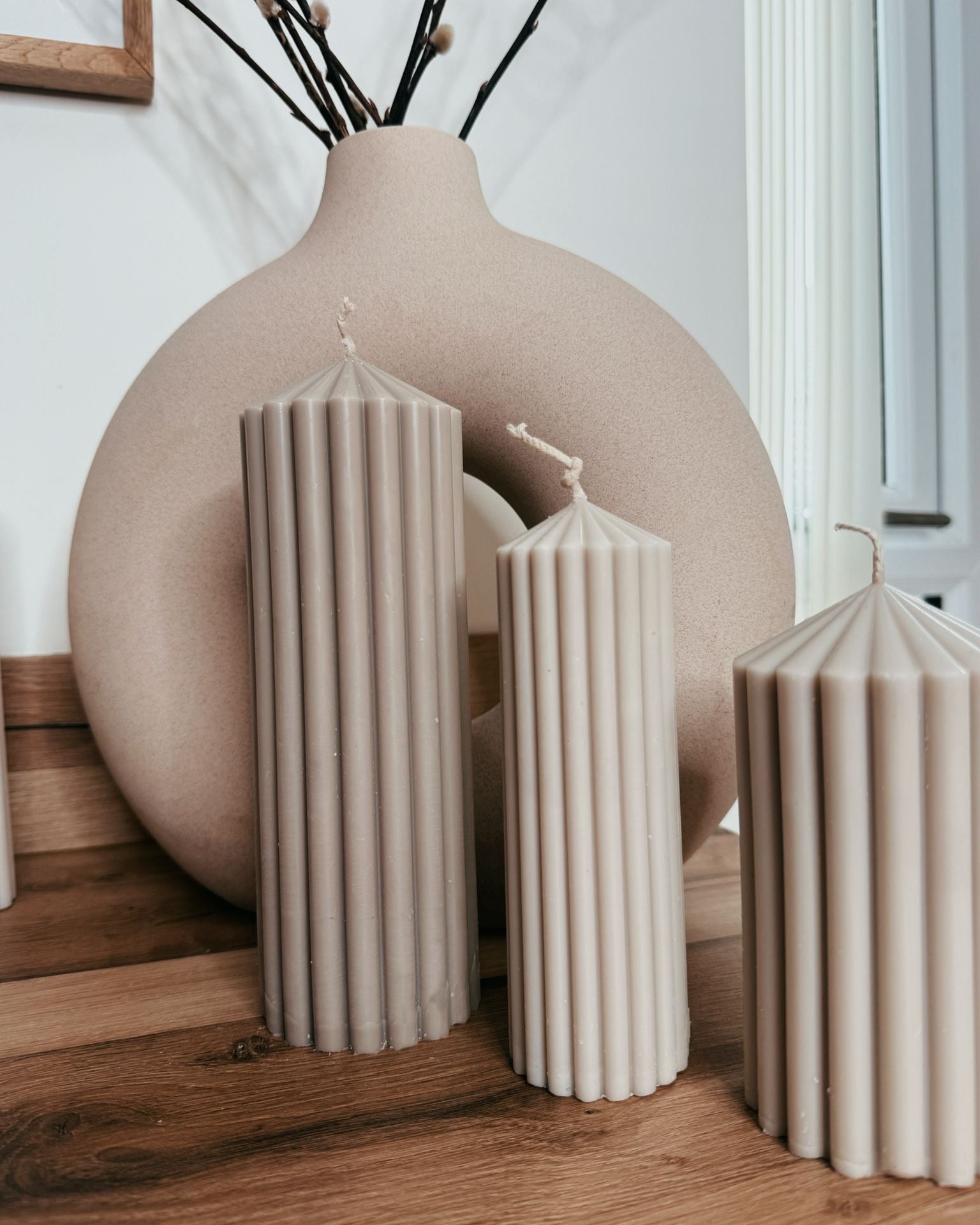 Set of beige candles and a large round vase on a wooden surface.
